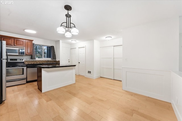 kitchen with light wood-type flooring, hanging light fixtures, and appliances with stainless steel finishes