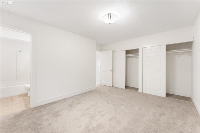 unfurnished bedroom featuring light colored carpet, ensuite bathroom, and multiple closets