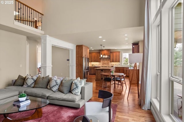 living area with recessed lighting, a high ceiling, light wood finished floors, and ornate columns