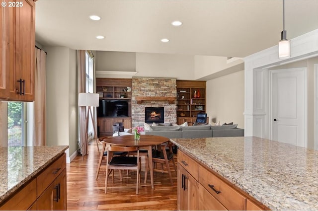 kitchen featuring recessed lighting, light wood-style floors, a stone fireplace, and light stone countertops