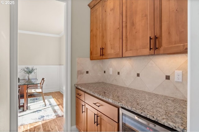 kitchen featuring beverage cooler, light stone countertops, crown molding, decorative backsplash, and wainscoting