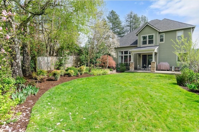 back of property with roof with shingles, a yard, and a patio