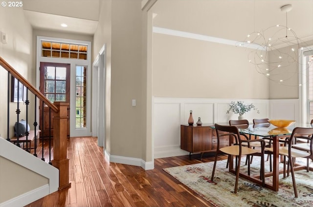 entryway featuring a decorative wall, wood finished floors, stairs, a wainscoted wall, and a notable chandelier
