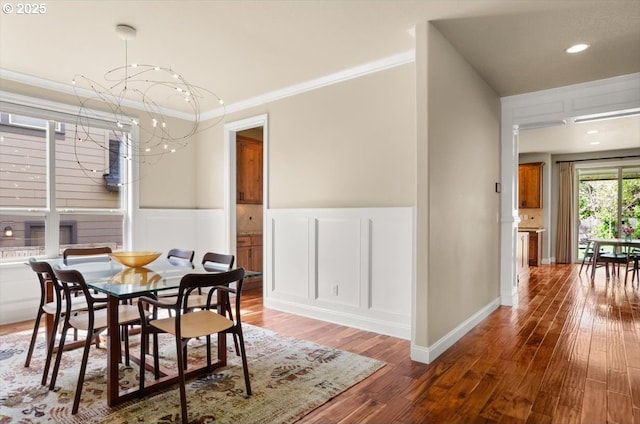 dining room featuring a decorative wall, a notable chandelier, hardwood / wood-style floors, a wainscoted wall, and ornamental molding