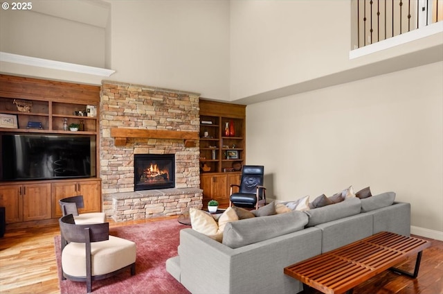 living room featuring built in shelves, a high ceiling, a stone fireplace, and light wood-style flooring