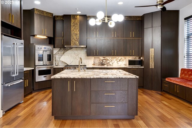 1716 NW Riverscape St, Portland, OR 97209 - kitchen with tasteful backsplash, wall chimney range hood, light wood-type flooring, dark brown cabinets, and stainless steel appliances