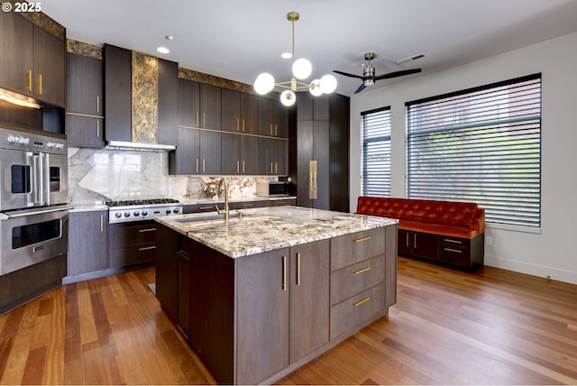 1716 NW Riverscape St, Portland, OR 97209 - kitchen featuring decorative backsplash, wall chimney range hood, appliances with stainless steel finishes, a sink, and light wood finished floors