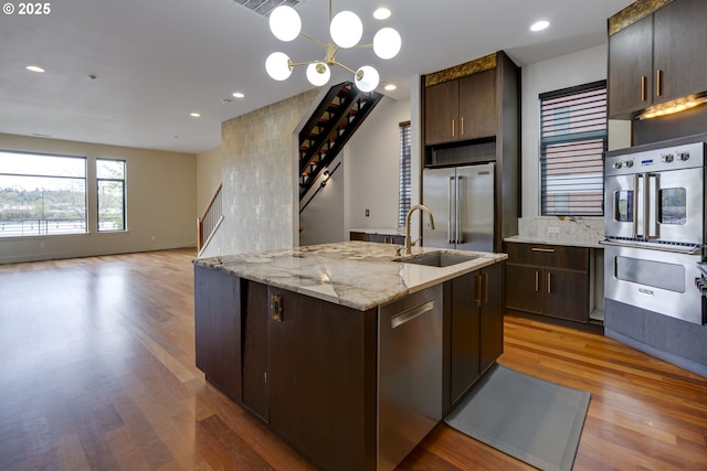 1716 NW Riverscape St, Portland, OR 97209 - kitchen featuring an island with sink, dark brown cabinetry, wood finished floors, a sink, and stainless steel appliances