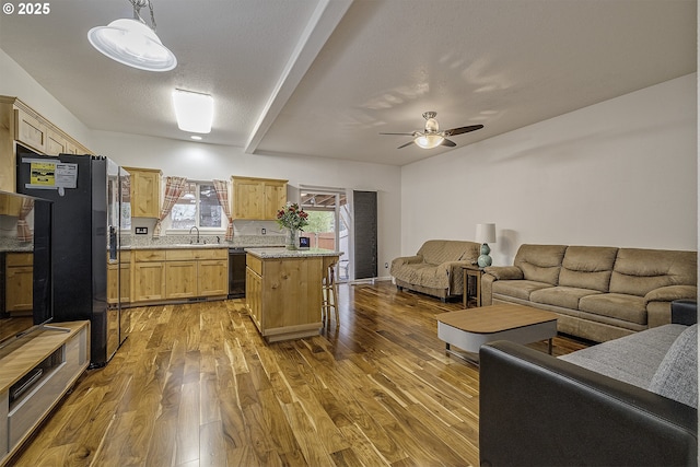 kitchen with light brown cabinetry, black dishwasher, wood finished floors, open floor plan, and freestanding refrigerator