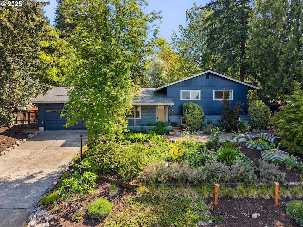 split level home with fence, an attached garage, brick siding, concrete driveway, and a garden