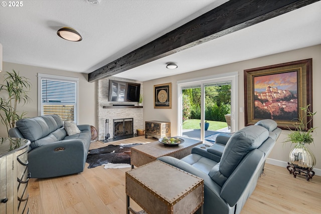 living room featuring a textured ceiling, a stone fireplace, baseboards, wood finished floors, and beamed ceiling
