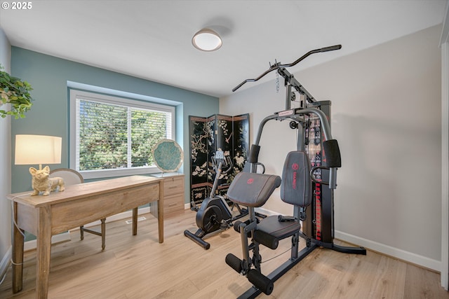 workout room featuring baseboards and light wood finished floors