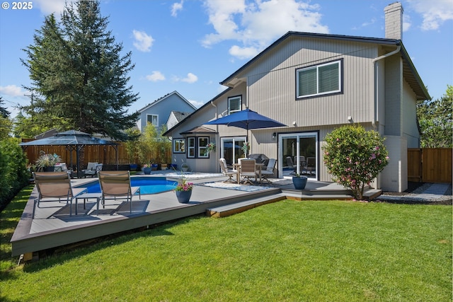 rear view of house featuring a chimney, a deck, a fenced in pool, a fenced backyard, and a yard