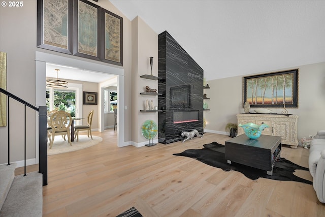 living area featuring an inviting chandelier, stairs, wood finished floors, baseboards, and high vaulted ceiling