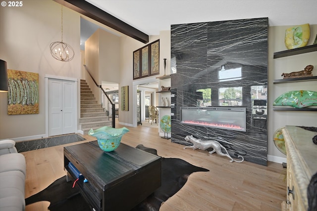 living room featuring a notable chandelier, stairs, wood finished floors, a high end fireplace, and beamed ceiling