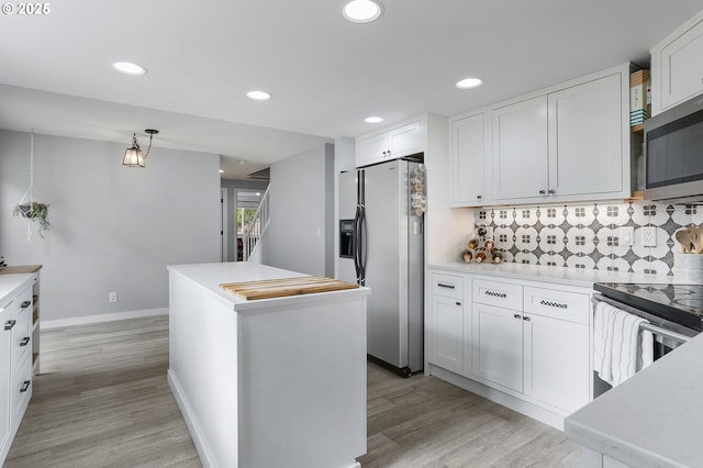 kitchen featuring stainless steel appliances, a kitchen island, white cabinets, light countertops, and backsplash