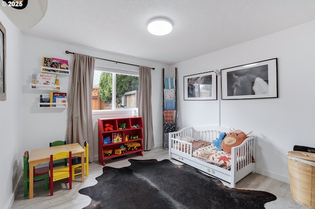 bedroom featuring a textured ceiling, a crib, wood finished floors, and baseboards