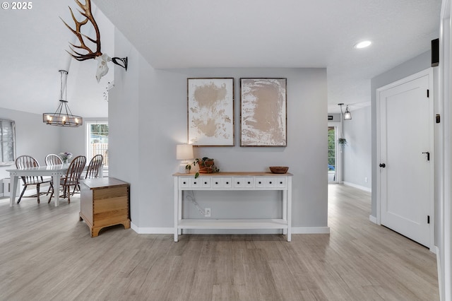 hall with light wood-type flooring, a notable chandelier, and baseboards