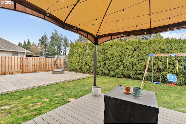 wooden deck with an outdoor fire pit, a playground, a lawn, and a fenced backyard