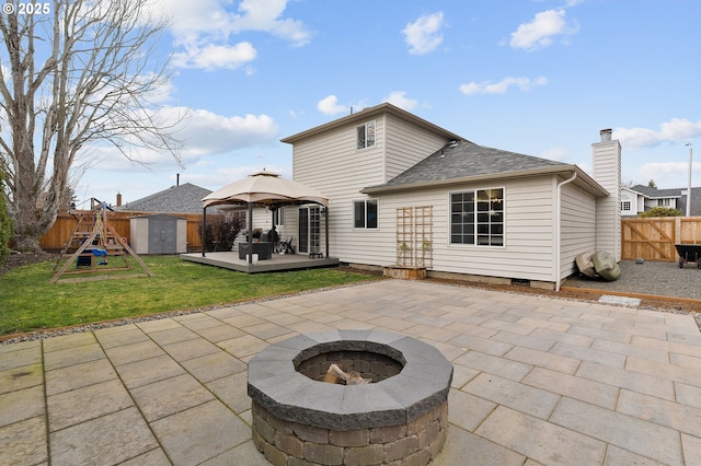 rear view of property featuring a storage shed, a fire pit, a patio, a fenced backyard, and an outdoor structure