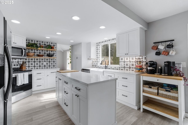 kitchen featuring light wood-style flooring, a sink, light countertops, appliances with stainless steel finishes, and open shelves