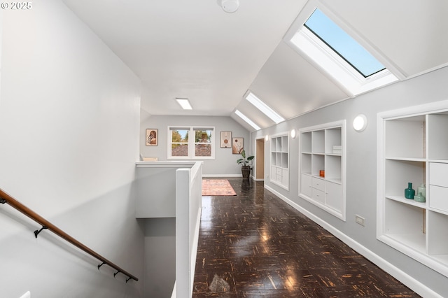 corridor with baseboards, an upstairs landing, built in shelves, and vaulted ceiling with skylight