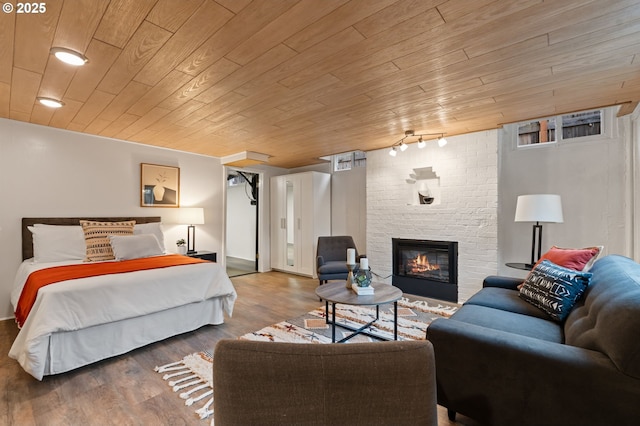 bedroom featuring wood finished floors, track lighting, wooden ceiling, and a fireplace