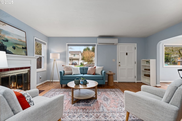 living area with wood finished floors, a fireplace, baseboards, and a wall mounted air conditioner