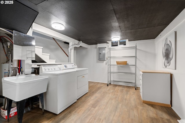 clothes washing area featuring washing machine and clothes dryer, electric panel, laundry area, light wood-style flooring, and a sink