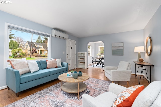 living area featuring arched walkways, a wealth of natural light, a wall unit AC, and wood finished floors