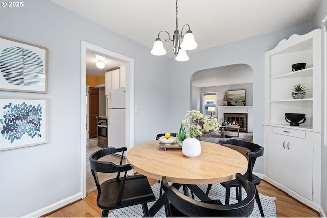 dining space with baseboards, light wood finished floors, an inviting chandelier, arched walkways, and a brick fireplace