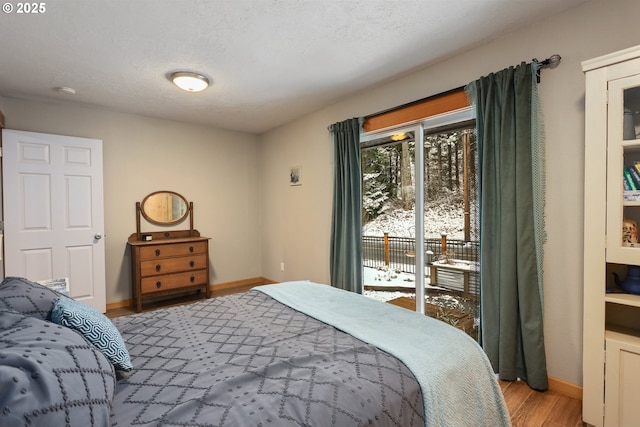 bedroom featuring access to exterior, light hardwood / wood-style floors, and a textured ceiling