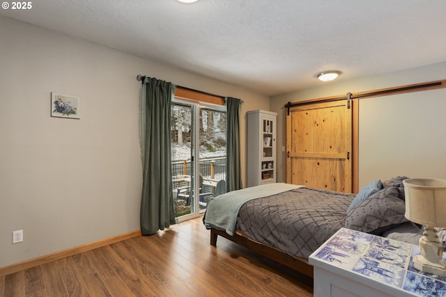 bedroom featuring hardwood / wood-style flooring, access to outside, a barn door, and a textured ceiling