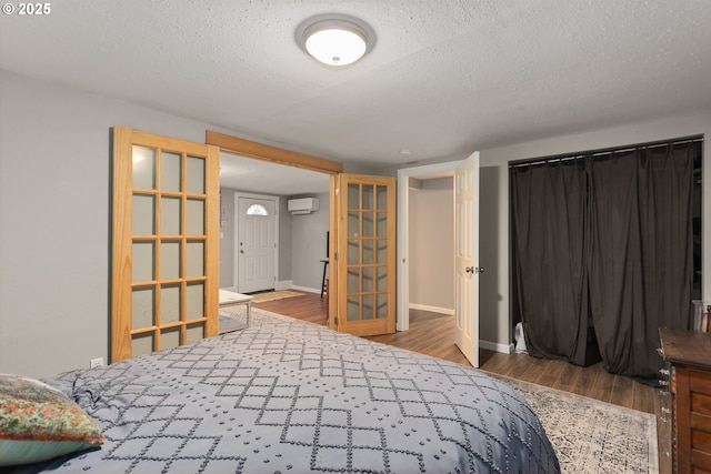 bedroom with a textured ceiling, wood-type flooring, french doors, and a wall mounted AC