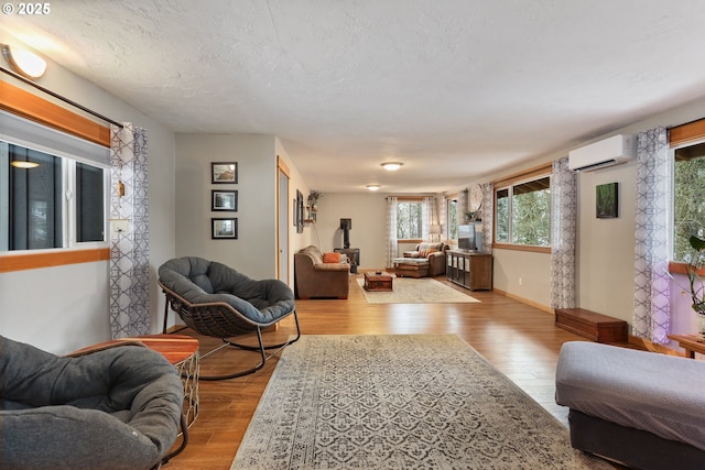 living room featuring a wall mounted AC, light hardwood / wood-style floors, and a textured ceiling