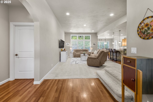 living area featuring arched walkways, baseboards, recessed lighting, and wood finished floors