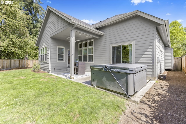 back of house featuring a hot tub, a fenced backyard, a lawn, a ceiling fan, and a patio