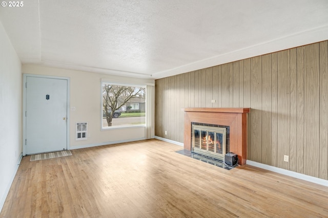 unfurnished living room with wooden walls, a textured ceiling, and light hardwood / wood-style floors