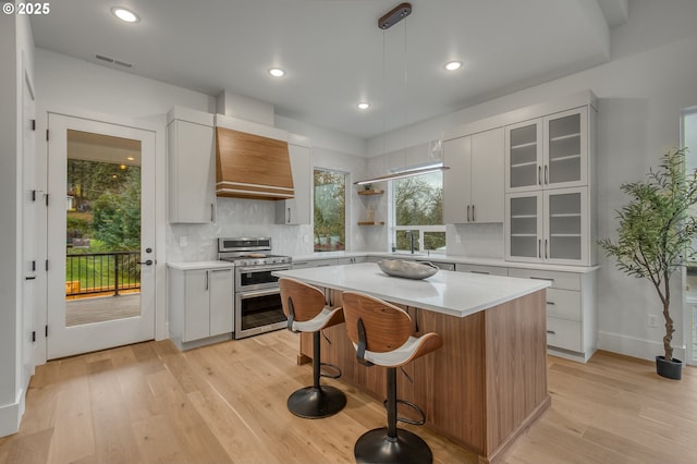 kitchen with custom exhaust hood, double oven range, a center island, white cabinetry, and hanging light fixtures