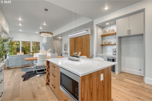 kitchen featuring a center island, stainless steel microwave, white cabinets, wine cooler, and decorative light fixtures