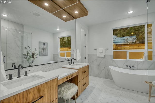 bathroom featuring vanity, a bath, and tile walls