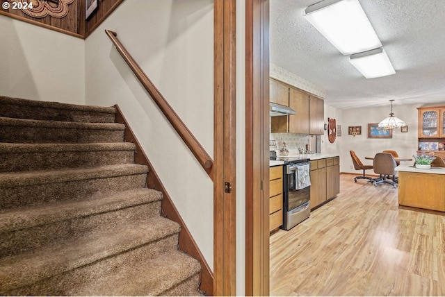 8050 SW 103rd Ave, Beaverton, OR 97008 - kitchen with stainless steel electric stove, a textured ceiling, light wood-style floors, light countertops, and under cabinet range hood