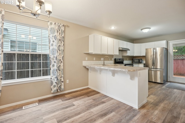 kitchen featuring appliances with stainless steel finishes, a breakfast bar area, white cabinets, hanging light fixtures, and kitchen peninsula