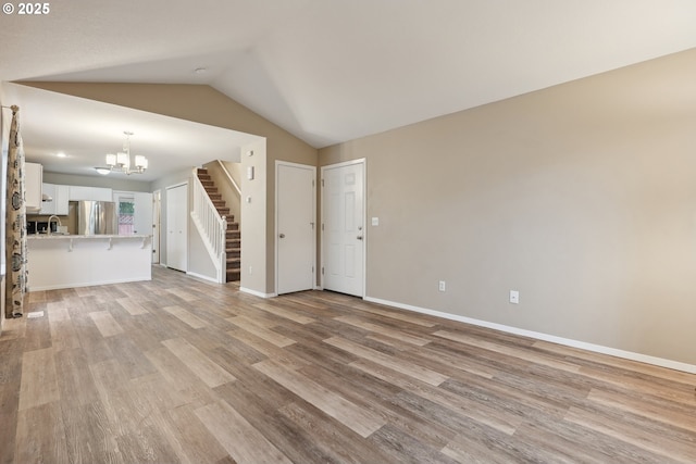 unfurnished living room with vaulted ceiling, a notable chandelier, and light hardwood / wood-style floors