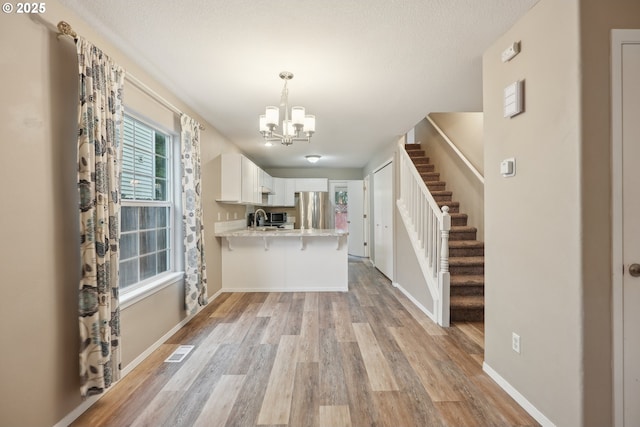 kitchen featuring sink, white cabinetry, stainless steel refrigerator, kitchen peninsula, and light hardwood / wood-style floors