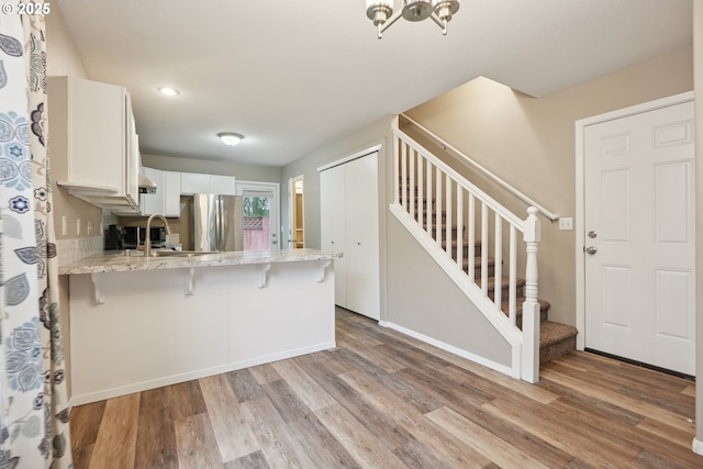 kitchen with a kitchen bar, white cabinetry, stainless steel refrigerator, kitchen peninsula, and light hardwood / wood-style floors