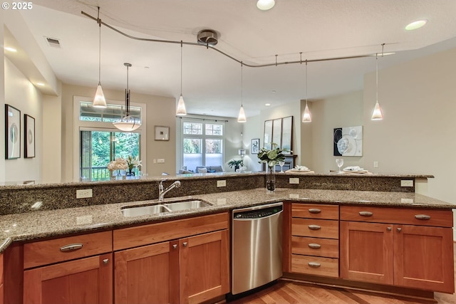 kitchen with dark stone countertops, sink, stainless steel dishwasher, and hanging light fixtures