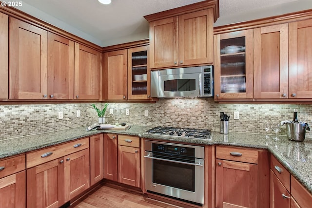 kitchen with stainless steel appliances, tasteful backsplash, stone counters, and light wood-type flooring