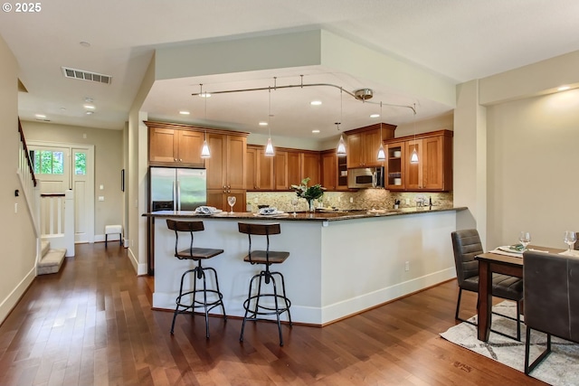 kitchen featuring dark wood-style floors, brown cabinetry, visible vents, stainless steel appliances, and dark countertops