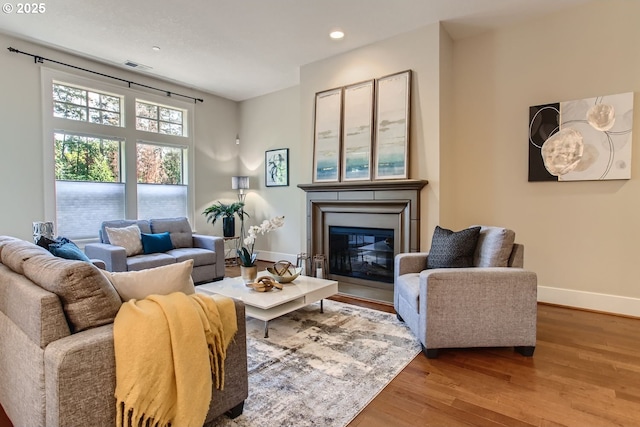 living room with wood finished floors, visible vents, baseboards, recessed lighting, and a glass covered fireplace